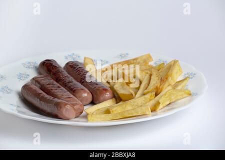 Teller mit hausgemachten Speisen mit Würstchen und langen Bratkartoffeln auf einem weißen Tisch Stockfoto