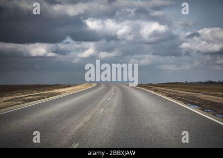 Natürliche Landschaft mit einer Asphaltstraße, die in Richtung Gewitterwolken führt. Stockfoto
