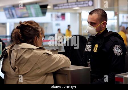 Beamte des US-amerikanischen Zoll- und Grenzschutzamtes für Feldeinsätze sehen internationale Passagiere aus, die am Dulles International Airport in Dulles, Virginia, am 13. März 2020 ankommen. Als Reaktion auf die Coronavirus-Pandemie (COVID-19) haben CBP-Beamte begonnen, persönliche Schutzausrüstung (PSA) zu tragen, während sie mit Passagieren interagieren, die aus dem Ausland ankommen. Viele Passagiere haben auch PSA gespendet, um sich und andere auf ihren Reisen zu schützen. Stockfoto