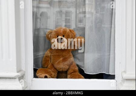 Der Teddybär, der aus einem Fenster rast und winkt, wartet darauf, dass ein vorbeigehendes Kind es bei der "Bärenjagd" während der Coronavirus-Pandemie findet. Stockfoto