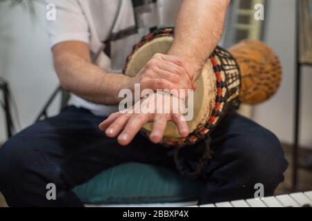Professionelle Musiker, die Schmerzen am Handgelenk haben, während sie djembe Musikinstrument im digitalen Studio zu Hause spielen. Er ist umgeben von Instrumenten und midi Co Stockfoto