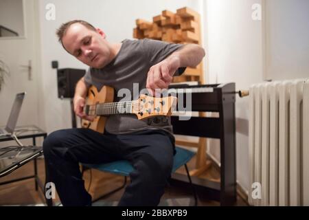 Professioneller Musiker, der E-Gitarre im digitalen Studio zuhause abstimmt. Er ist umgeben von Instrumenten und midi-Controller. Musikproduktion kon Stockfoto