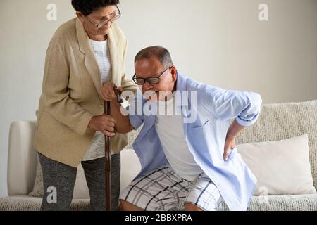 Asiatische alte Frau hilft einem älteren Mann, der Rückenschmerzen hat, Rückenschmerzen zu Hause. Konzept für das Gesundheitswesen. Stockfoto