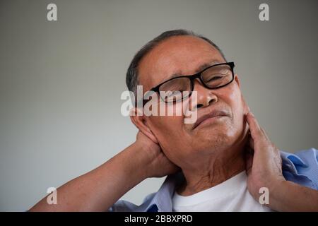 Asiatischer alter Mann sitzt auf dem Sofa und hat Nackenschmerzen, Rückenschmerzen zu Hause. Konzept für das Gesundheitswesen. Stockfoto
