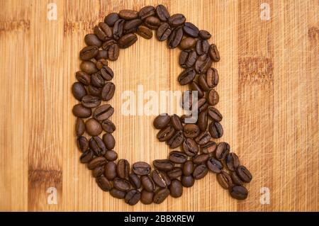 Buchstaben Q aus gerösteten Kaffeebohnen, 3D-Rendering auf Holztischhintergrund Stockfoto