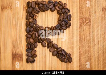 Buchstaben R aus gerösteten Kaffeebohnen, 3D-Rendering auf Holztischhintergrund Stockfoto