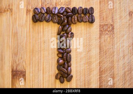 Buchstaben T aus gerösteten Kaffeebohnen, 3D-Rendering auf Holztischhintergrund Stockfoto