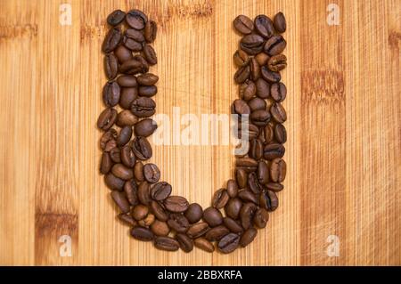 Buchstaben U aus gerösteten Kaffeebohnen, 3D-Rendering auf Holztischhintergrund Stockfoto