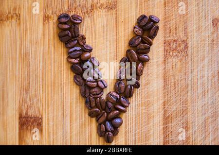 Buchstaben V aus gerösteten Kaffeebohnen, 3D-Rendering auf Holztischhintergrund Stockfoto