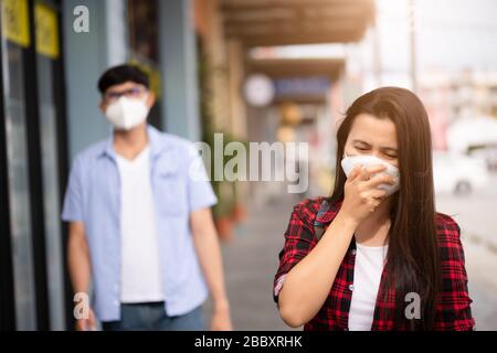 Nahaufnahme von Frau und Mann, die eine Gesichtsmaske und Husten tragen, machen Sie sich bereit für Coronavirus und 2,5 Uhr kämpfen beim Aufwachen des Einkaufszentrums im Freien Stockfoto