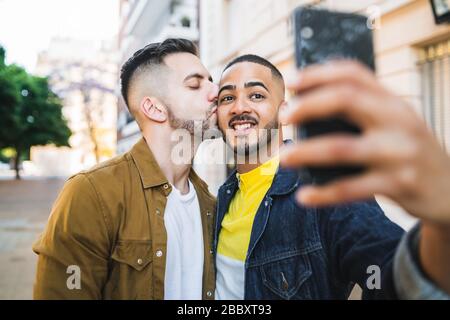 Porträt des fröhlichen schwulen Paares, das Zeit zusammen verbringt und ein selfie mit Handy auf der Straße mitnimmt. LGBT und Love Konzept. Stockfoto