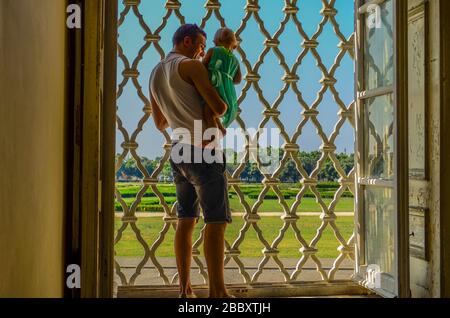 Ein junger Vater mit einem kleinen Mädchen in den Armen, der durch das Fenster blickt Stockfoto