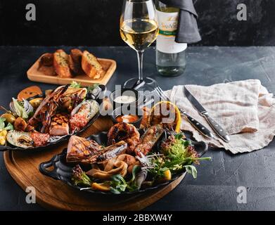 Verschiedene Meeresfrüchte auf Teller. Schöne Komposition auf einem Tisch mit Meeresfrüchten, Tintenfisch, Garnelen, Lachssteak und Tintenfisch. Lebensmittelfoto, niedrige Tonart, traditionell Stockfoto