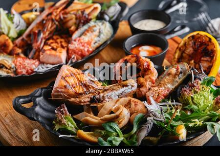 Verschiedene Meeresfrüchte auf Teller. Schöne Komposition auf einem Tisch mit Meeresfrüchten, Tintenfisch, Garnelen, Lachssteak und Tintenfisch. Lebensmittelfoto, niedrige Tonart, traditionell Stockfoto
