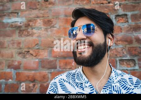 Jungen gutaussehenden Mann, der Sommer Kleidung und Musik hören mit Kopfhörern gegen die Mauer. Urban Konzept. Stockfoto