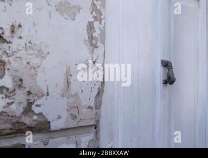 Weiße Tür mit eisernem Klopfer, wie eine Hand und eine alte zerbrochene Wand Stockfoto