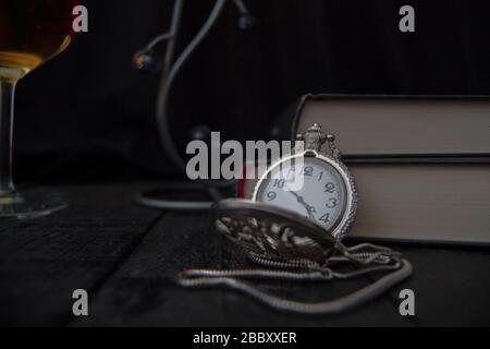 Taschenuhr auf einigen Büchern platziert. Im Hintergrund ein Glas Wein. Stockfoto