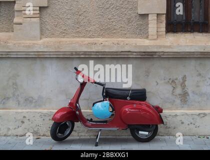 Rotes vespa-motorrad mit blauem Helm vor einem hundertjährigen Gebäude geparkt Stockfoto