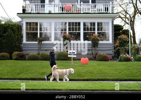 Portland, USA. April 2020. Ein junger Mann läuft seinen Hund vor einem Haus, das ein "allein zusammen"-Zeichen neben einem Herzen in Portland, Ore., am 1. April 2020 zeigt, während die Menschen weiterhin soziale Distanzierungsmaßnahmen in Verbindung mit einem landesweiten Stay-at-home-Verfahren praktizieren, um die Verbreitung des neuartigen Coronavirus zu verlangsamen. (Foto von Alex Milan Tracy/Sipa USA) Credit: SIPA USA/Alamy Live News Stockfoto