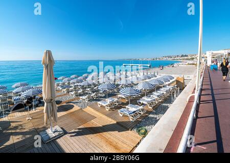 Touristen gehen an der Promenade des Anglais entlang des Strandes, der Bucht der Engel und einem privaten Ferienclub an der französischen Riviera in Nizza, Frankreich. Stockfoto