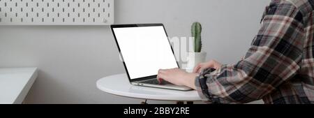 Freiberufliche Freiberuflerin, die auf einem Laptop mit leerem Bildschirm auf einem weißen Kreistisch mit Kaktuskanne arbeitet, hat einen zugeschnittenen Schuss gemacht Stockfoto