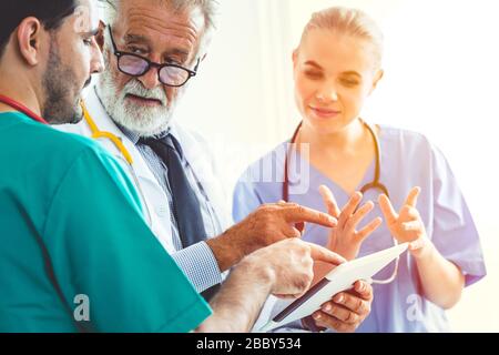 Arzt/Ärzte-Team-Diskussion über Patientenfall mit Tablet- oder Handheld-Monitor-Bildschirm. Stockfoto