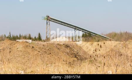 Förderband einer Sand- und Schotteranlage in der Nähe von München. Hügel mit Erde im Vordergrund. Sand- und Schotterbergbau. 16:9 Panoramaformat. Stockfoto