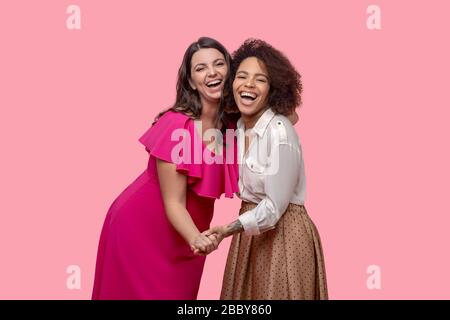 Zwei fröhliche Freundinnen umarmen sich von Angesicht zu Angesicht und halten Hand. Stockfoto