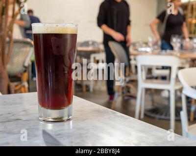 Dunkles Bier, das auf dem Tisch im Restaurant sitzt, und die Gäste sitzen Stockfoto