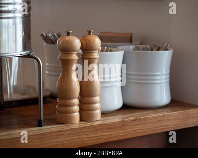 Holzhandkurbel mit Salz und Pfefferschüttler auf dem Tisch mit Utensilien in Keramiktöpfen Stockfoto