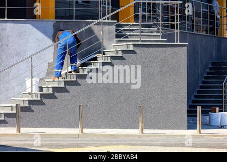 Arbeiter in blauen Overalls setzen dekorativen Fassadenputz an die Wand des Gebäudes. Stockfoto