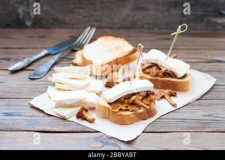 Zwei Bruschetten mit brie- und Chantillenpilzen, auf Holztisch mit Gabel und Messer auf weißer Serviette Stockfoto