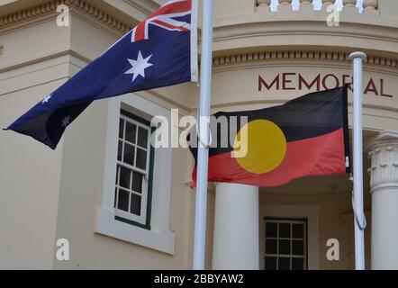 Flagge der Aborigines, die neben der australischen Nationalflaggen vor einer Gedenkhalle in der regionalen Stadt fliegt Stockfoto