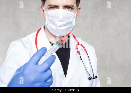 Doktor hält eine Spritze in der Hand, die mit roter Flüssigkeit gefüllt ist, Konzept der Blutentnahme oder des Impfstoffs Stockfoto