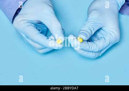 Doktor hält gelbe Pillen in den Händen. Medizinischer Arbeiter in Handschuhen. Pharmakologie. Blauer Hintergrund Stockfoto