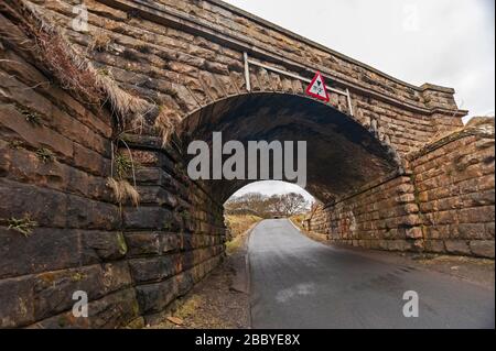 Alte steinerne Eisenbahnbrücke mit niedrigen Warnung Zeichen über einen Feldweg Stockfoto