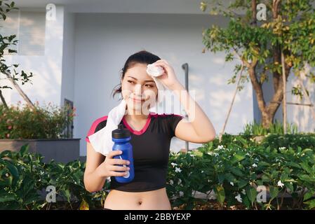 Atemberaubende Fitness Asian Frau wischt Schweiß und hält eine Flasche Wasser nach dem Joggen oder laufen im Freien Stockfoto