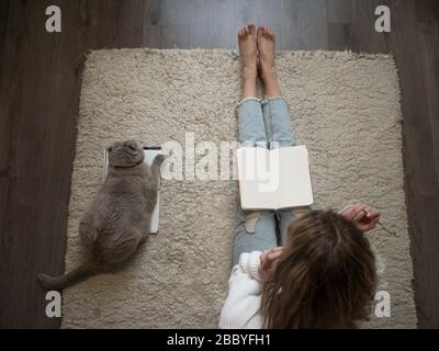 Planen Sie Dinge, setzen Sie Ziele. Eine junge Frau sitzt auf dem Boden auf dem Teppich und schreibt in ein Tagebuch. Behalten Sie einen Gewohnheits-Tracker. Stockfoto