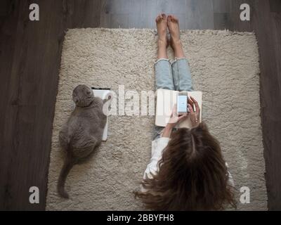 Planen Sie Dinge, setzen Sie Ziele. Eine junge Frau sitzt auf dem Boden auf dem Teppich und schreibt in ein Tagebuch. Behalten Sie einen Gewohnheits-Tracker und verwenden Sie die App auf dem Smartphone. Stockfoto