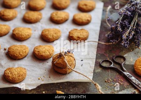 Frisch gebackene herzförmige Plätzchen auf Pergamentpapier, Lavendelblüte. Stockfoto