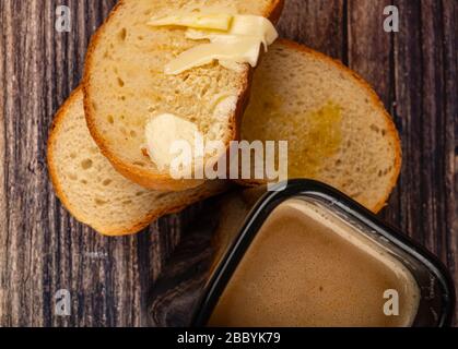 Frischer Weizentoast mit Butter und einem Keramikbecher mit Kaffee mit Milch auf Holzgrund. Nahaufnahme Stockfoto