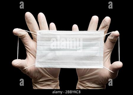 Arzt mit medizinischer Gesichtsmaske, Atemverband in zwei Händen in weißen Handschuhen isoliert auf schwarzem Hintergrund. Konzept der globalen Auswirkungen von COVID-19 Stockfoto
