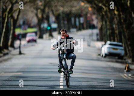 Radfahrer macht während des Corona-Virus-Lockdowns einen Roller auf einer ruhigen Glasgower Straße. Stockfoto