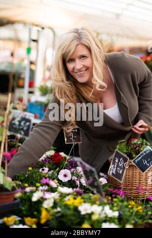 Attraktive Frau mittleren Alters kauft sich auf einem Markt glücklich Blumen Stockfoto