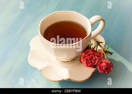 Nachmittagstee in weißem Klassiker mit Rosen auf blauem Holzhintergrund Stockfoto