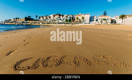 Leerer idyllischer Sandstrauch Praia do Ribeiro in Cascais, Portugal mit den Worten Cascais auf Sand geschrieben - Weitwinkel Stockfoto