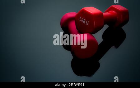 Rote und dunkelrosafarbene Hanteln isoliert auf schwarzem Hintergrund. 2, 3 kg Hanteln. Geräte für Krafttraining. Trainingszubehör für das Bodybuilding. Ausrüstung Stockfoto