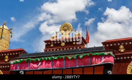 Goldenes Dharma-Rad und Hirsche auf dem Dach des Jokhang-Tempels. Die acht Speichen des Rades stellen den achtfachen Weg dar. Blauer Himmel mit weißen Wolken Stockfoto