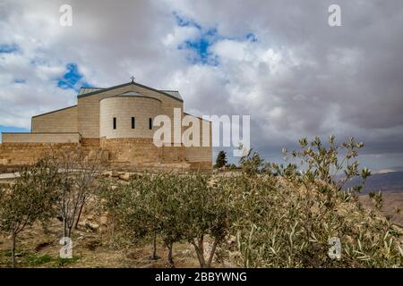 Memorial Basilica of Moses, Mount Nebo, Königreich Jordanien, bewölkt eindrucksvoller Himmel Winternachmittag. Olivenbäume im Vordergrund, Performance von Natur und Architektur Stockfoto
