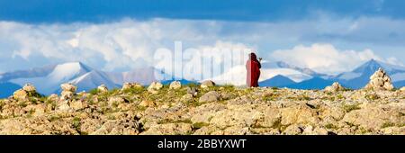 Panorama der Landschaft in der Nähe des Nam Tso Sees. Mit schneebedeckten Bergen und einer Pilgerin (Frau) mit roter Robe. Der See ist ein heiliger Ort für den tibetischen buddhismus Stockfoto